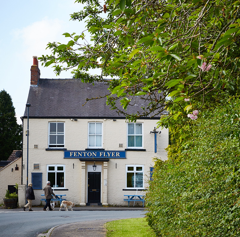 The Fenton Flyer on Main Street in Church Fenton, framed by leafy trees.